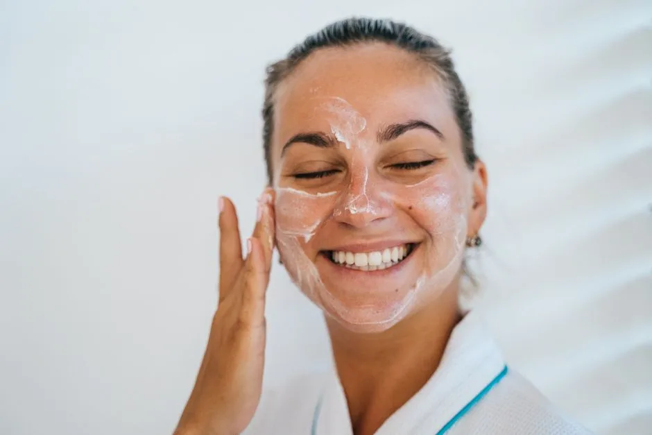 Close-up of a woman smiling while applying facial cream, promoting skincare.