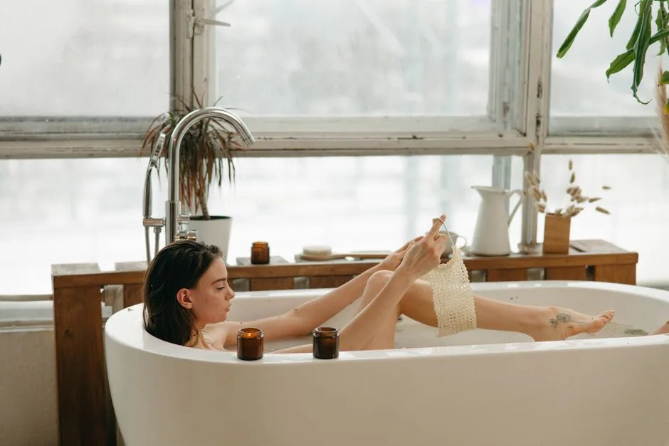 Woman in a bathtub with candles, relaxing and using a body scrub. Cozy indoor setting.
