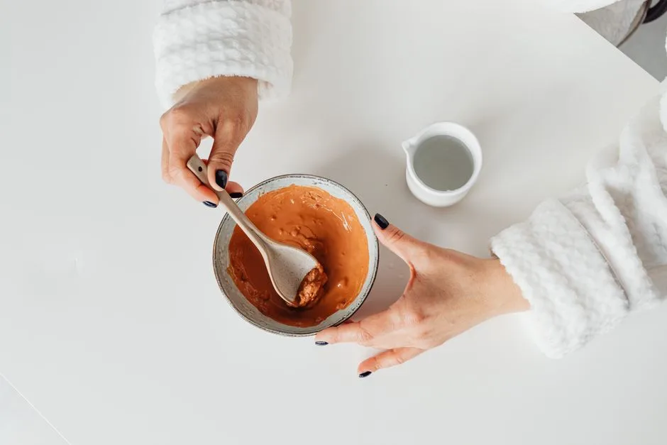 Woman in bathrobe mixing homemade clay mask in a bowl, ideal for skincare DIY concepts.
